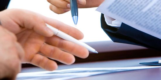 two people with pen and paper in hands reviewing documents
