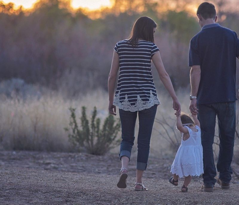 parents holding young daughters hands as she walks