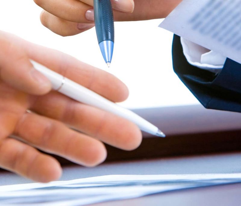 two people with pen and paper in hands reviewing documents